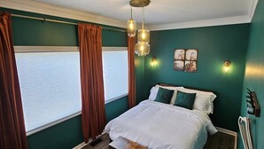 Un dormitorio con una cama grande, un banco de madera, una ventana con cortinas y una lámpara de pared.