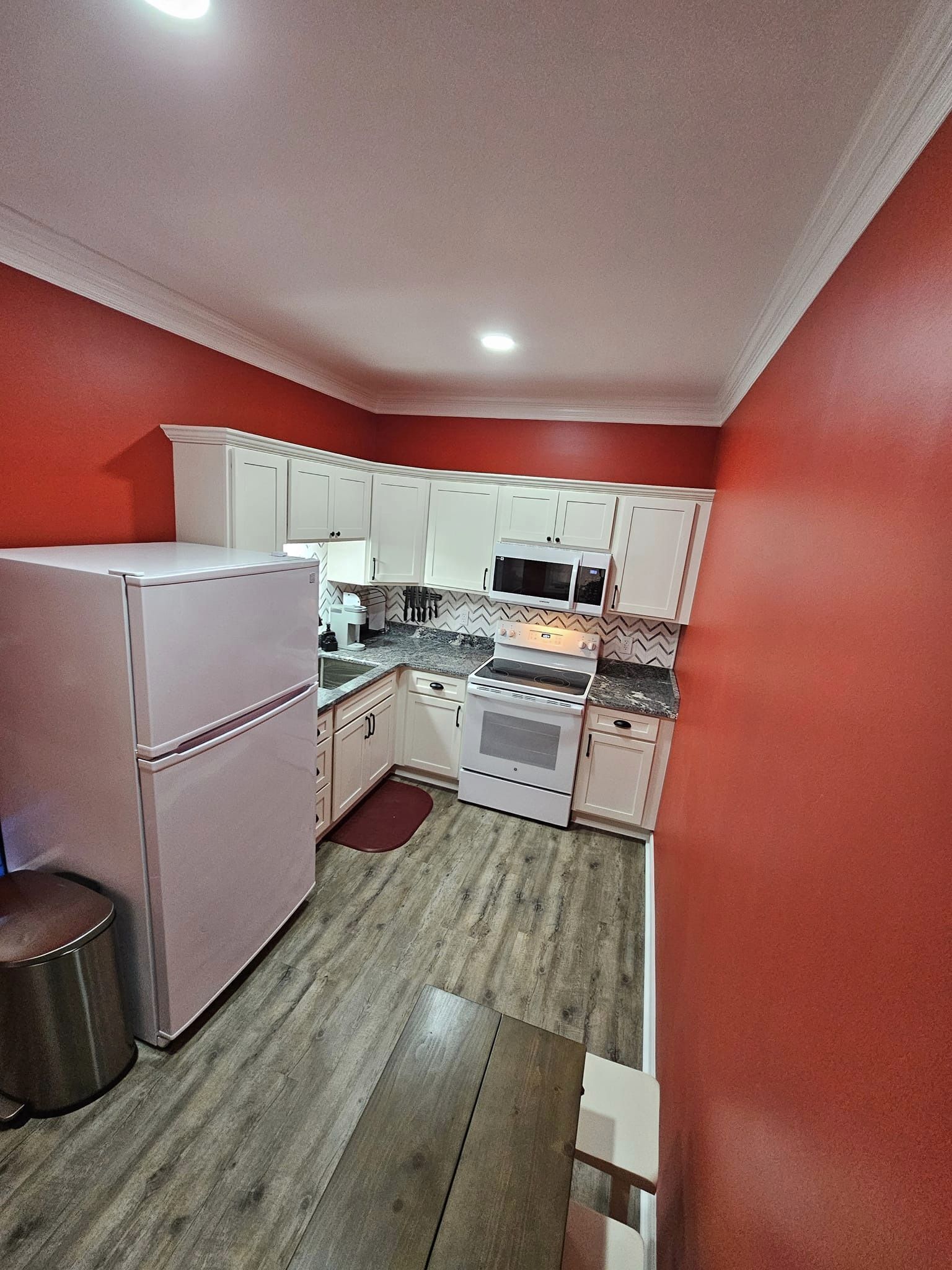 Une cuisine de taille réduite avec des meubles blancs, un réfrigérateur, un four à micro-ondes et une cuisinière.