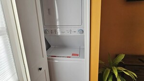 Un lavadero con lavadora y secadora de carga frontal, una planta en maceta y un banco de madera.