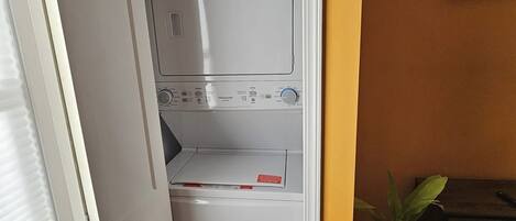 Un lavadero con lavadora y secadora de carga frontal, una planta en maceta y un banco de madera.