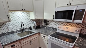 Una cocina con armarios blancos, microondas, estufa y pileta.