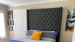 A bedroom with a tufted headboard, a grey and blue bedspread, and a wooden floor. - Terrific 4-bedroom house in Tylertown with WiFi, AC (Tylertown)