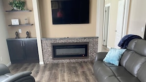 A living room with a flat-screen TV mounted above a fireplace, leather sofas, and a dark wood floor. - Terrific 4-bedroom house in Tylertown with WiFi, AC (Tylertown)