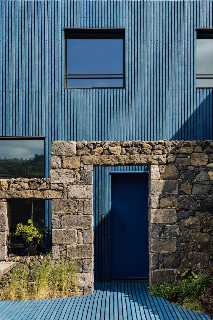 A modern building with a blue exterior, a stone archway, and a blue door.