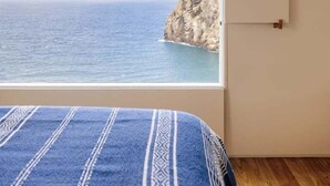 A bedroom with a large window overlooking a coastal view.