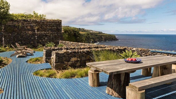 A wooden deck with a stone wall and a table with a fruit bowl.