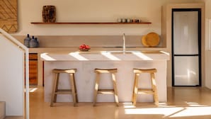 A modern kitchen with a central island, bar stools, a refrigerator, and decorative items on shelves.