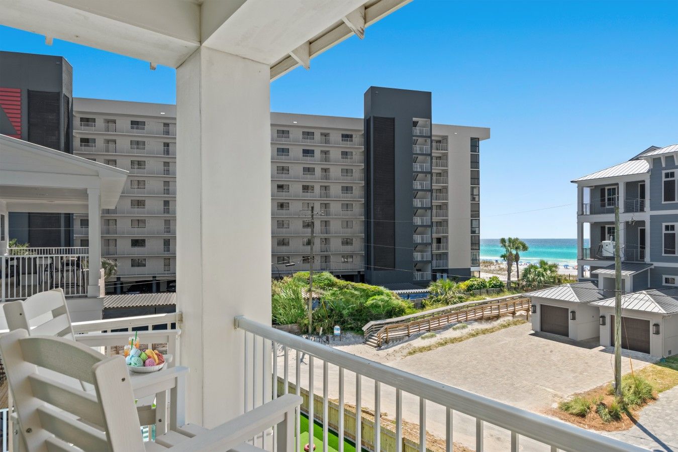 A balcony with a view of a beach and ocean, a building with multiple balconies, and a clear sky.