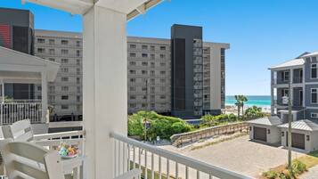 A balcony with a view of a beach and ocean, a building with multiple balconies, and a clear sky.