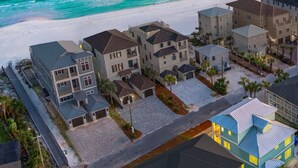 A coastal residential area with multiple two-story houses, a paved driveway, and a beach in the background. - Few steps across from beach, Gulf views, Saltwater pool, Golf cart (Miramar Beach)