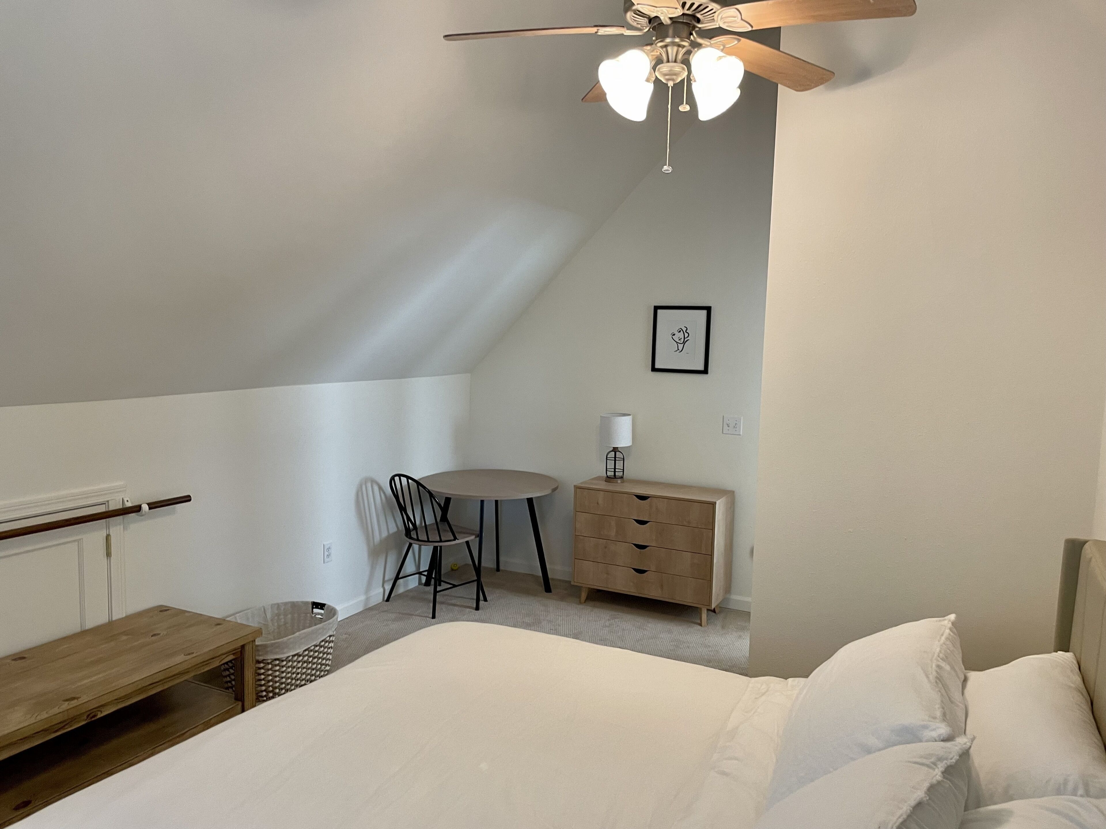 Un dormitorio con cama, escritorio, silla, cómoda de madera y ventilador de techo.