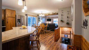 A modern kitchen with wooden cabinets, a large island, and a dining area with chairs. - Lakeside Bliss: Ideal Rental on Potato Lake close to Downtown Park Rapids  (Park Rapids)