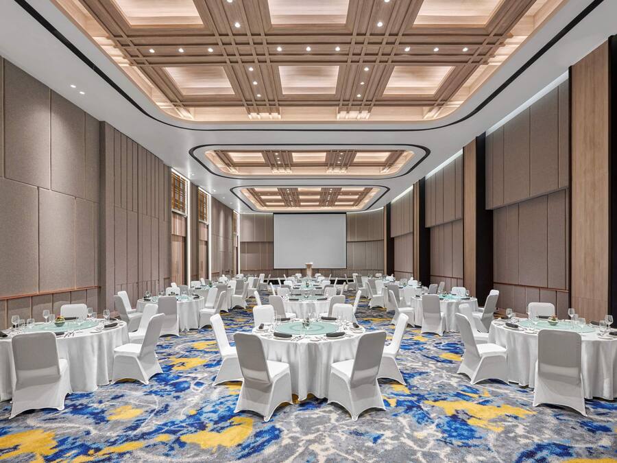 Une salle de conférence avec des tables rondes, des chaises blanches et un tapis bleu à motifs.