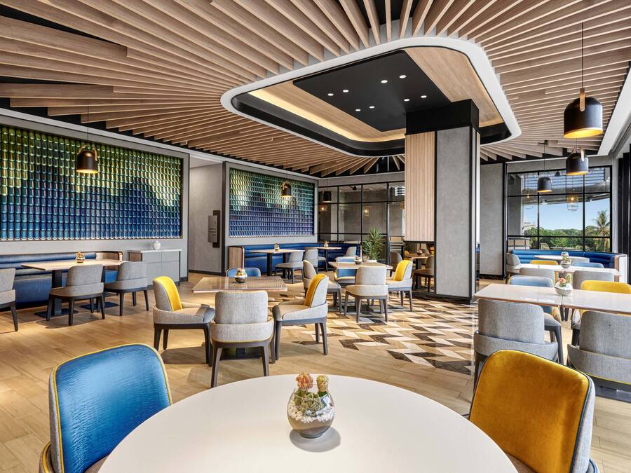 Un restaurante moderno con diversas opciones de asientos, incluyendo mesas redondas y cabinas, y un suelo con diseño.