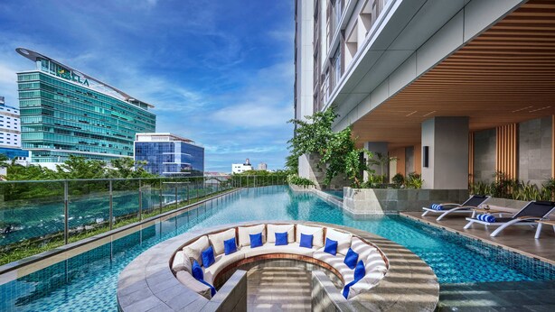 A rooftop infinity pool with a curved seating area, surrounded by modern buildings and a clear sky. - Hyatt Place Makassar (Makassar)