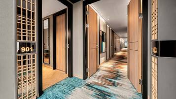 Un pasillo moderno de hotel con paneles de madera, puertas numeradas y una alfombra estampada.