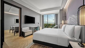 Una habitación de hotel moderna con una cama grande, un escritorio, una silla, un televisor y vistas a la ciudad.