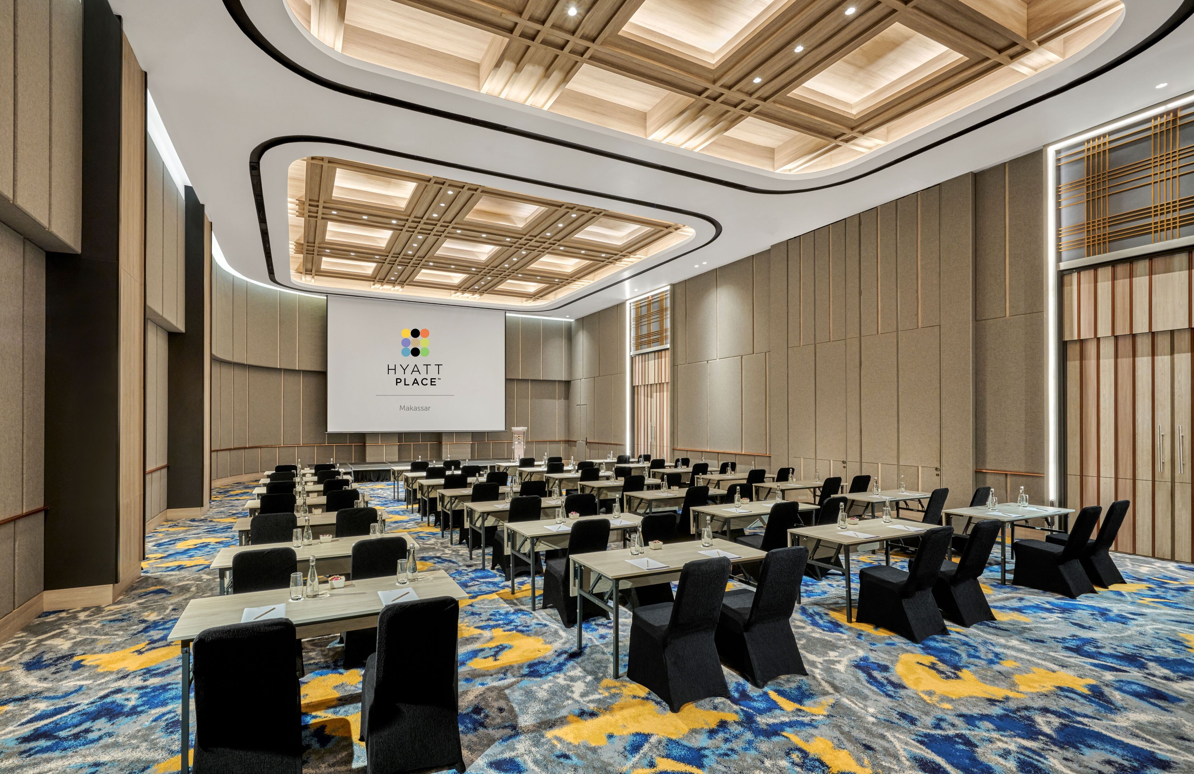 A conference room with a modern design, featuring a large screen, multiple tables, and chairs arranged for a meeting.