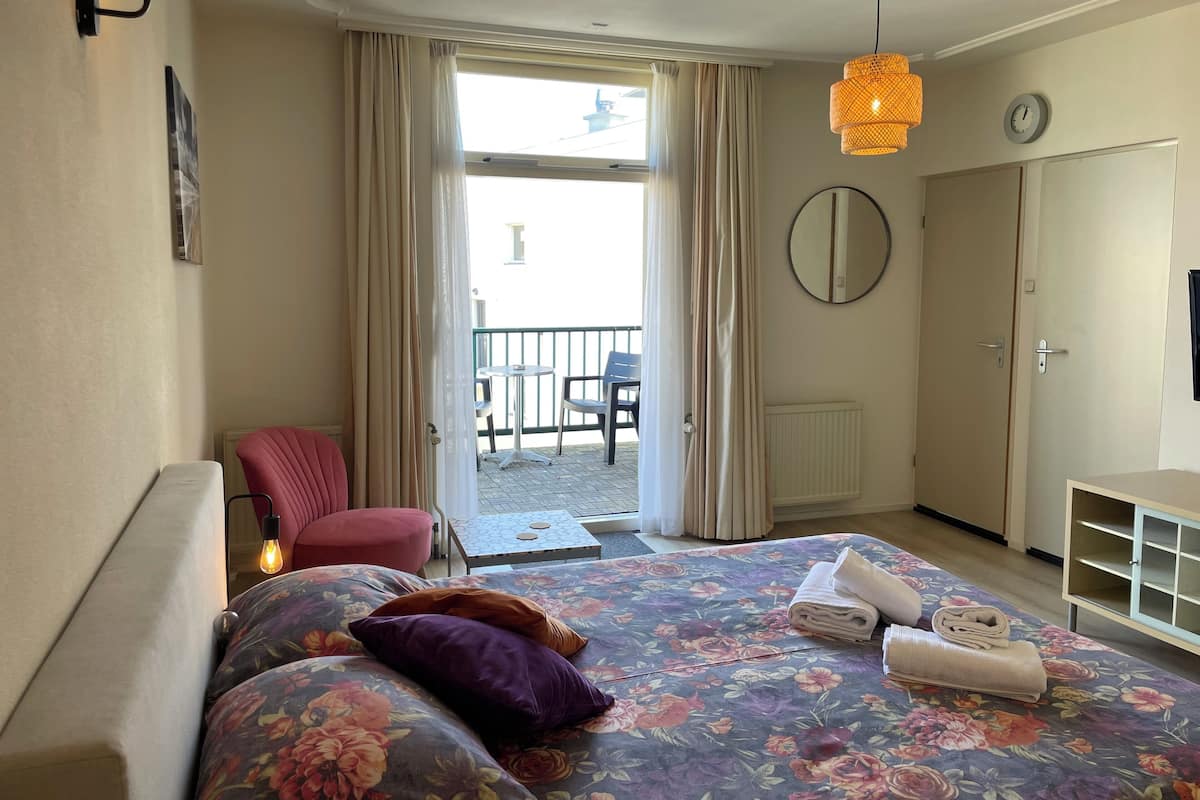 A hotel room with a bed, a chair, a desk, a wardrobe, and a balcony.