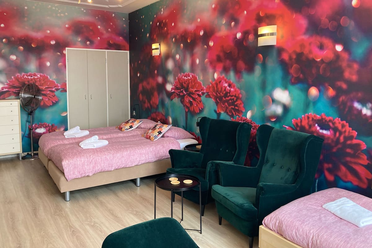 A bedroom with a bed, two chairs, a small table, a wardrobe, and a wall with a floral mural.