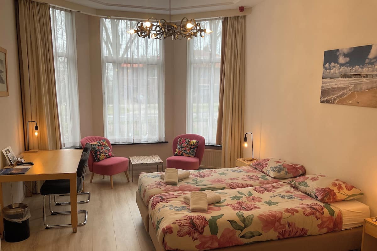 A hotel room with a bed, two chairs, a desk, a small table, and a window with curtains.