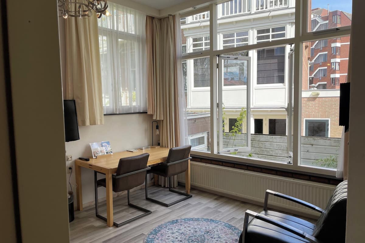 A room with a wooden table, two chairs, a TV, and a large window with a view of buildings.