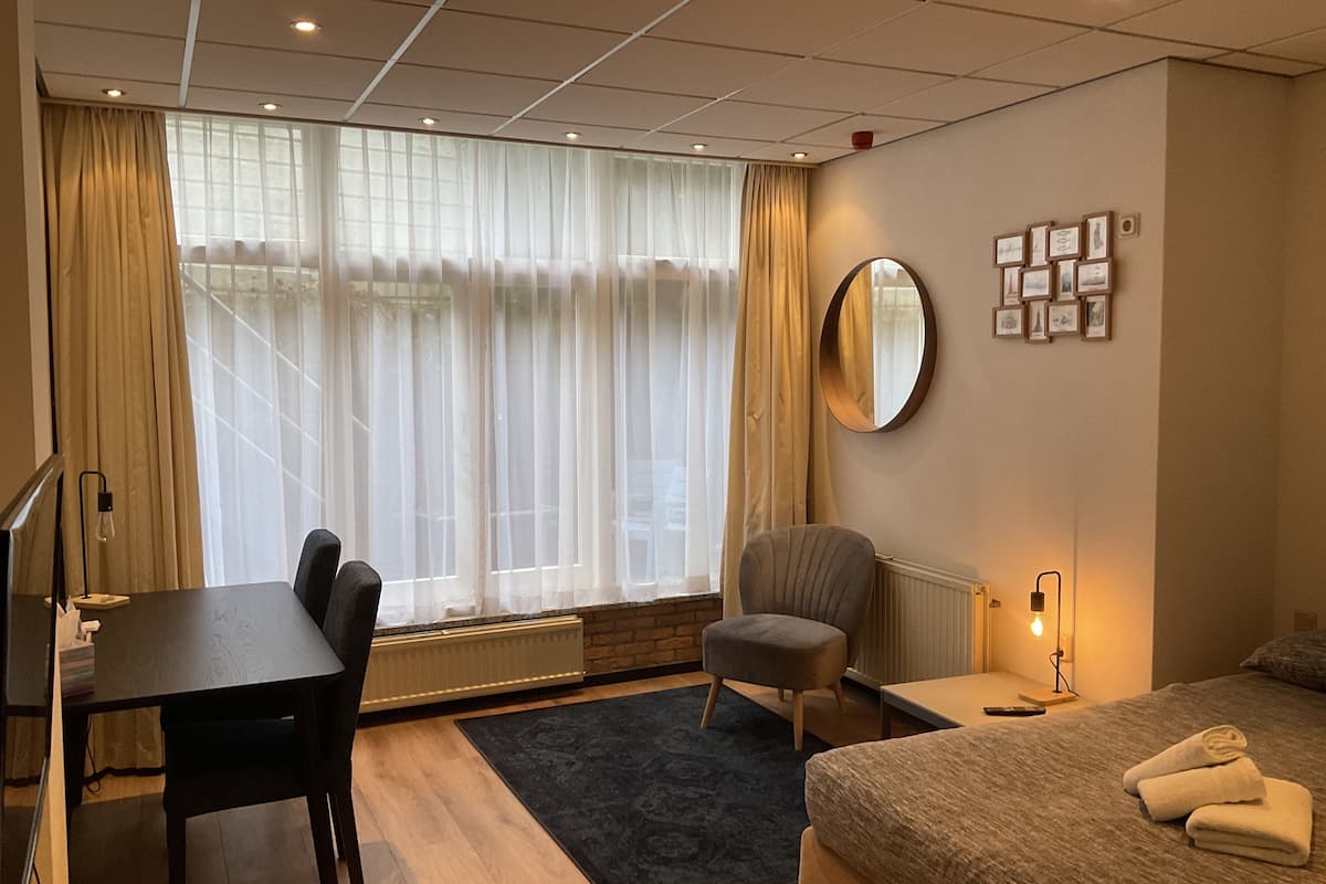 A hotel room with a bed, a desk, a chair, a round mirror, and a wall with framed pictures.