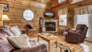 A cozy cabin interior with wooden walls, a fireplace, a sofa, a chair, and a table. - Cozy 2BR/2BA Cabin, Sleeps 6 w Hot Tub & Indoor Pool in Gated Resort (Sevierville)