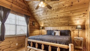 A wooden cabin bedroom with a bed, a nightstand, a lamp, and a ceiling fan. - Cozy 2BR/2BA Cabin, Sleeps 6 w Hot Tub & Indoor Pool in Gated Resort (Sevierville)