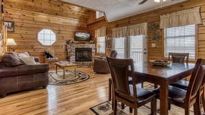 A cozy log cabin interior with a fireplace, wooden dining table, and comfortable seating. - Cozy 2BR/2BA Cabin, Sleeps 6 w Hot Tub & Indoor Pool in Gated Resort (Sevierville)