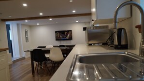 Ett modernt kök med en diskho i rostfritt stål, en kaffebryggare och en tv i bakgrunden.