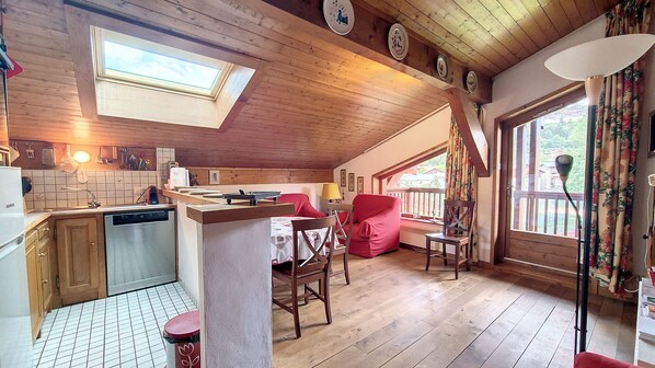 A cozy kitchen with a dining area, wooden floors, and a view through large windows.