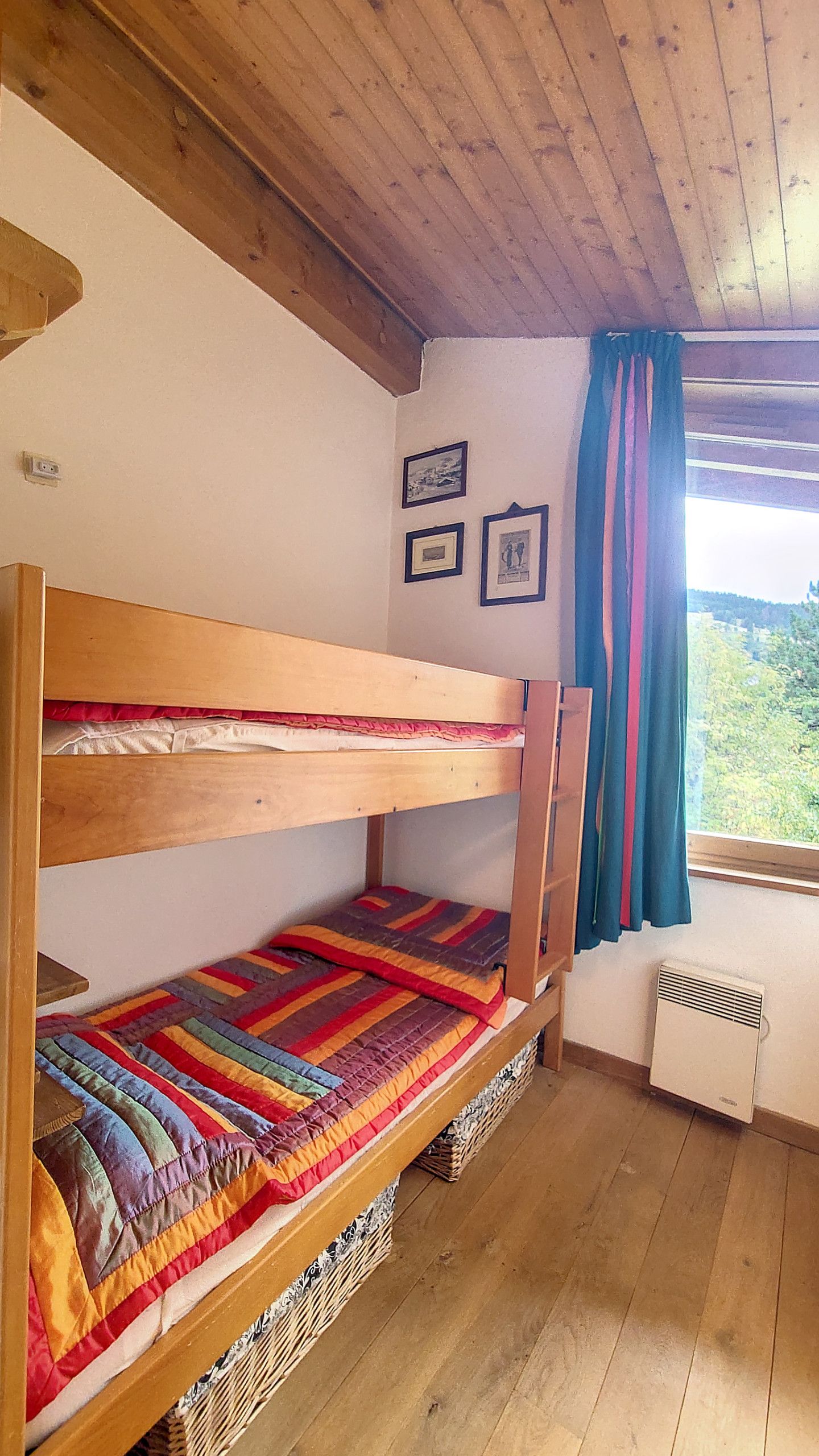 Un lit superposé avec une courtepointe aux couleurs vives, une petite fenêtre avec des rideaux et un climatiseur fixé au mur.