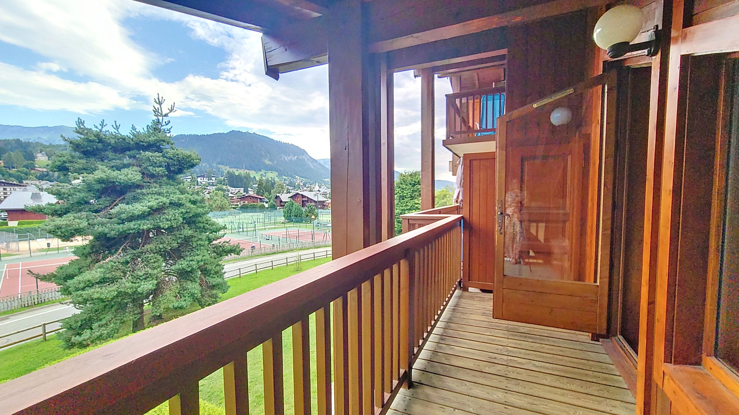 A wooden balcony with a view of a tennis court and surrounding greenery.