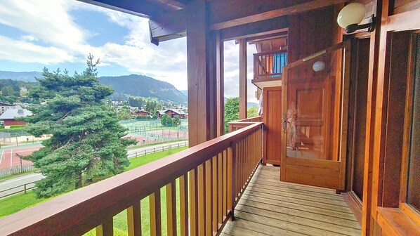 A wooden balcony with a view of a tennis court and surrounding greenery.