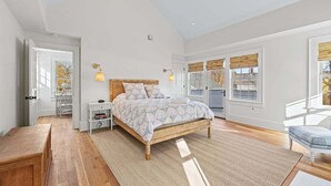 Une chambre avec un grand lit, des tables de chevet, un banc et une vue sur l’extérieur.