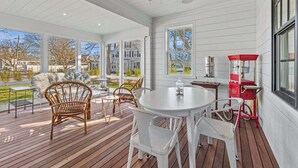 Un patio couvert avec une table et des chaises, un fauteuil en osier et un appareil électroménager rouge.