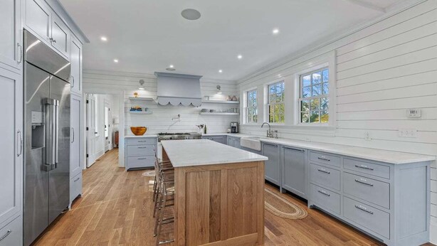 Une cuisine moderne avec des meubles blancs, un îlot central en bois et une grande fenêtre qui laisse entrer la lumière naturelle.