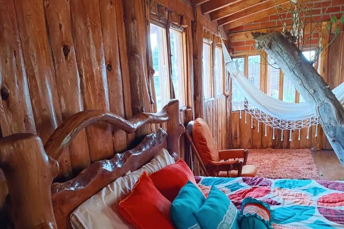 A rustic wooden room with a bed, a hammock, and a wooden headboard.