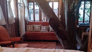 Habitació rústica de fusta amb un llit gran, un sofà vermell i una finestra amb vistes.