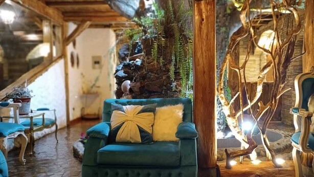 Una habitació acollidora amb un sofà blau, bigues de fusta i una petita cascada interior.
