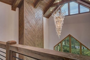 Un interior moderno con una pared de madera en patrón de espiga, una lámpara colgante y vistas a través de un ventanal triangular.