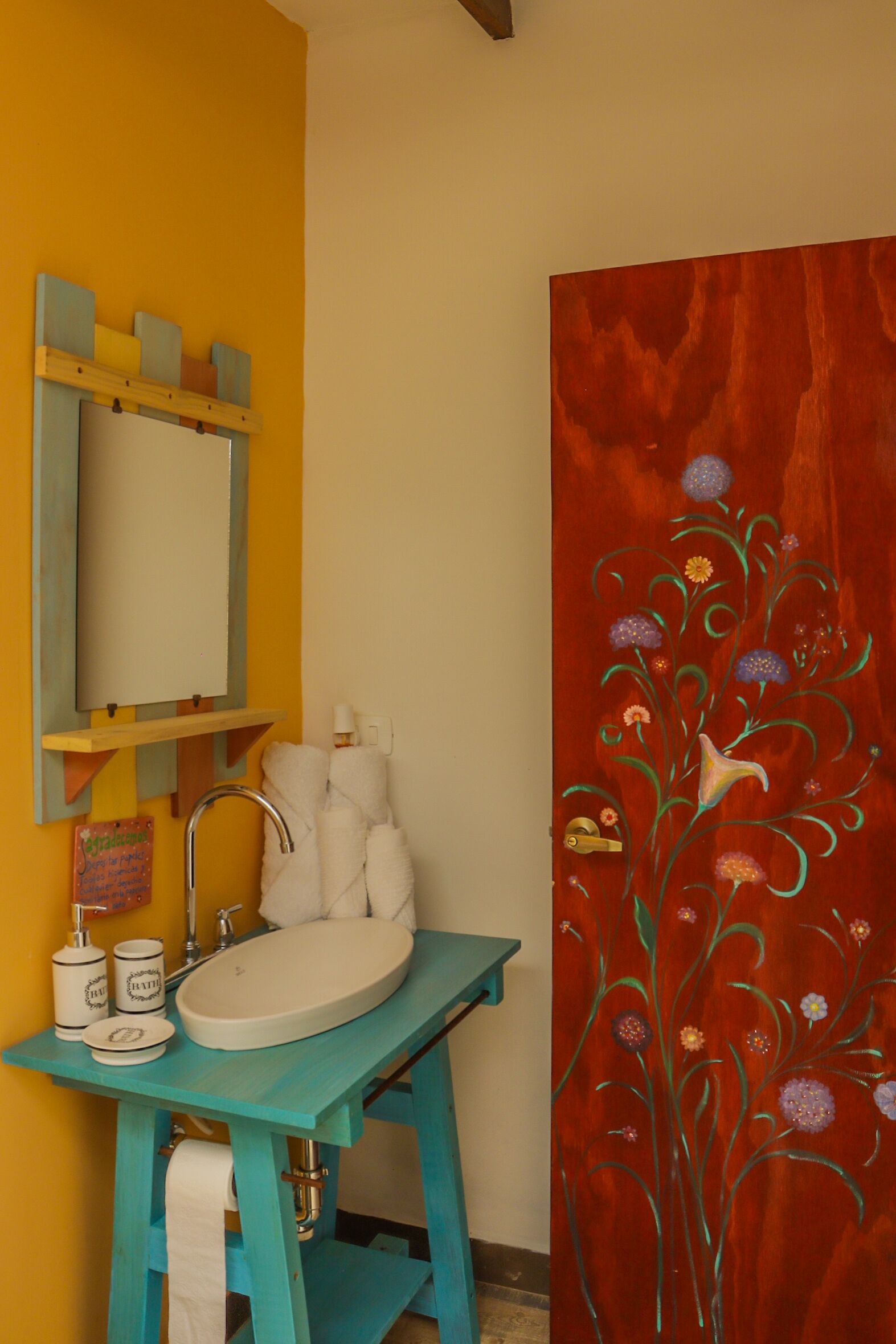 A bathroom with a turquoise sink, a mirror, and a decorative red panel with floral designs.