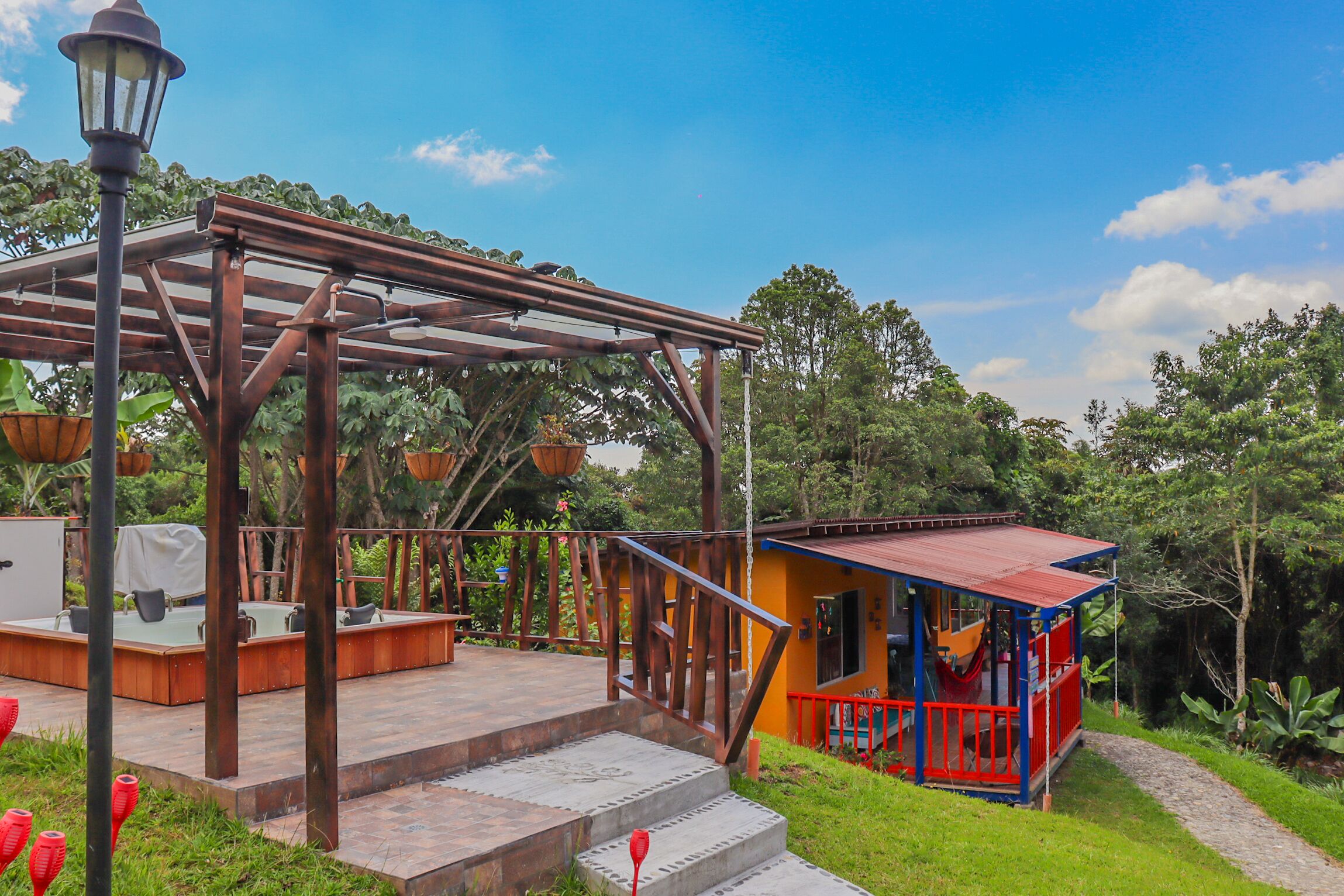 A wooden deck with a metal pergola, a small outdoor seating area, and a colorful building with a red railing.