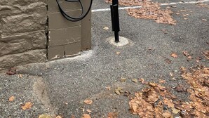 Un espace de stationnement équipé d’une borne de recharge, un mur en pierre et un sol recouvert de feuilles.