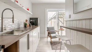 Une cuisine moderne dotée d’un évier en acier inoxydable, d’une machine à café intégrée et d’un coin repas avec une chaise et une table.