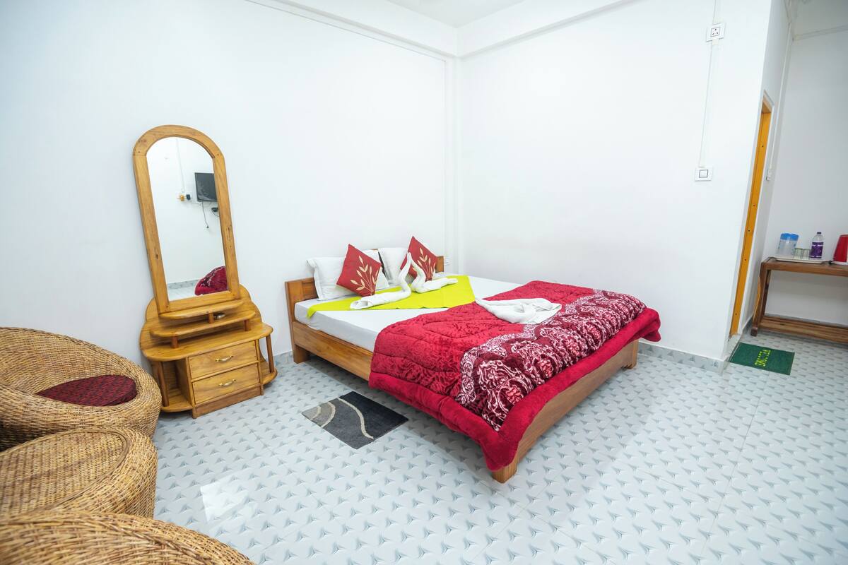 A neatly arranged bedroom with a bed, a wooden dresser, a mirror, and wicker chairs.