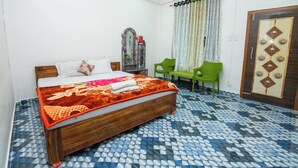 A neatly arranged bedroom with a wooden bed, a green chair, and a patterned floor. - Jungle Star Mansion (Bokakhat)
