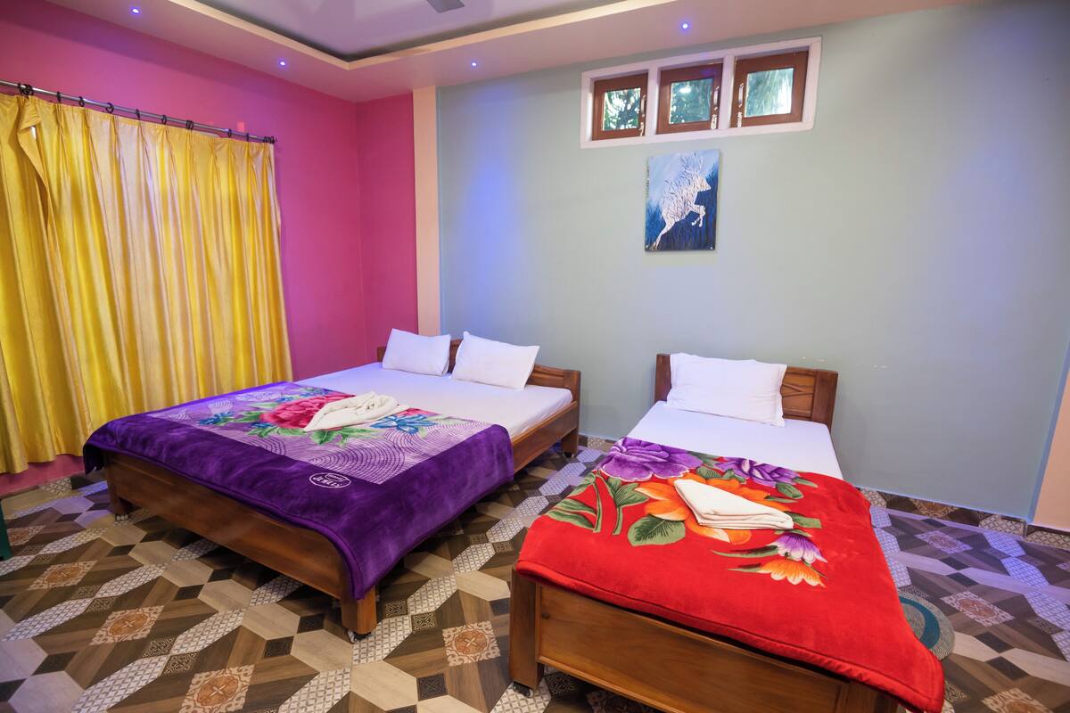 A hotel room with two beds, a patterned floor, a painting on the wall, and a window with a view of trees.