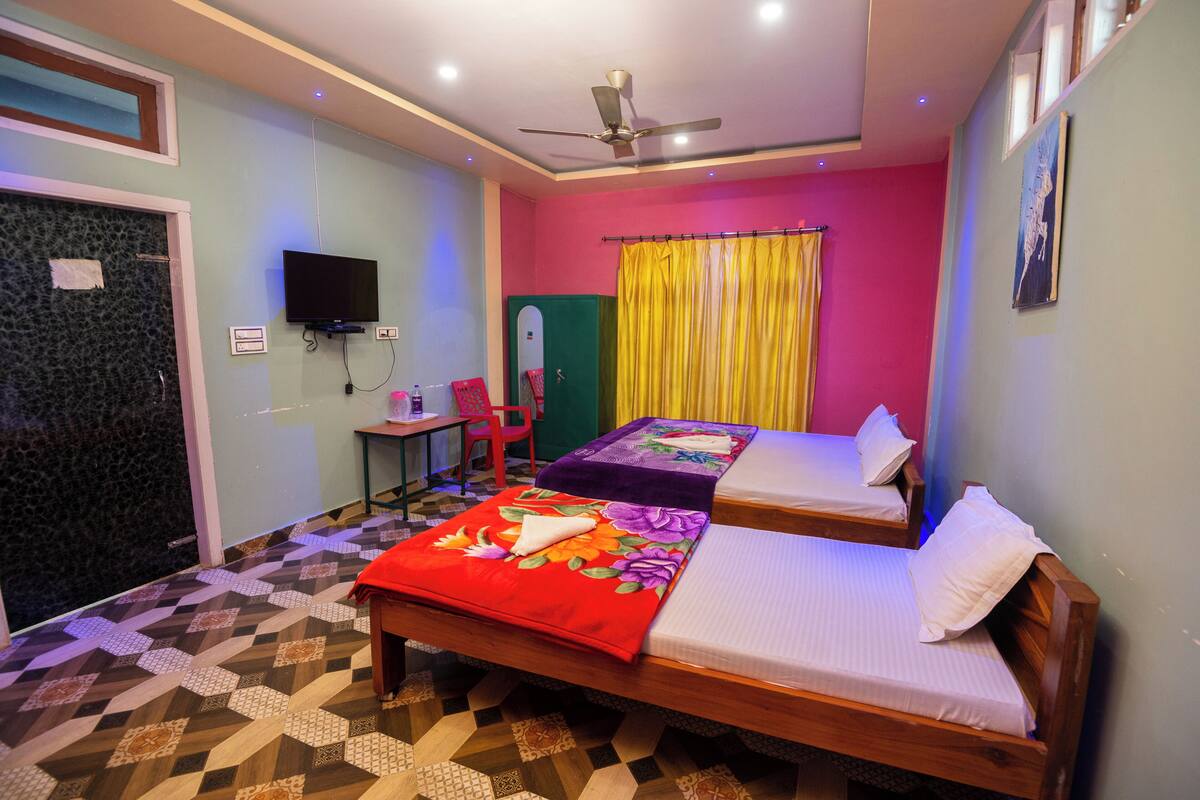 A room with two beds, a ceiling fan, a TV, and a desk with a chair.